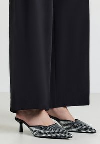 Mules à bout pointu en satin noir ornés d'un motif éblouissant de strass, avec un talon aiguille fin et un design à dos ouvert.