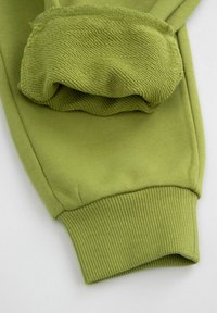 Zielona bawełniana tkanina z elastycznym mankietem i teksturowaną nakładką na rękawie. Gładka powierzchnia z żebrowanym dolnym brzegiem.