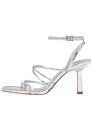 Sandales à talons hauts métalliques argentées avec lanière à la cheville, bout ouvert, et talon aiguille fin. Présentent un design croisé.