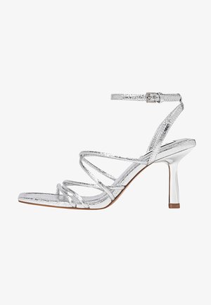 Sandales à talons hauts métalliques argentées avec lanière à la cheville, bout ouvert, et talon aiguille fin. Présentent un design croisé.