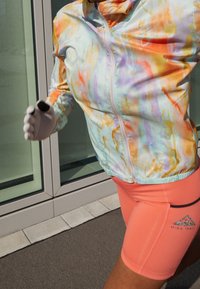 Barevná, lehká bunda s vířivým vzorem v pastelových odstínech. Slučuje se s růžovými úzkými šortkami s logem. Hladká textura, atletický střih.