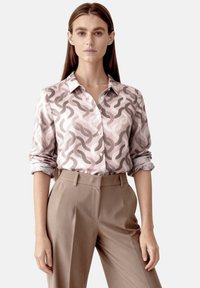 Button-up shirt in soft, pink fabric with a wavy abstract pattern, paired with high-waisted, beige trousers, featuring a tailored fit.