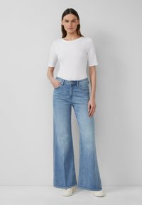 Jeans in denim blu chiaro a gamba larga con vita alta, abbinati a una maglietta aderente bianca a maniche corte. Texture liscia e design classico a cinque tasche.