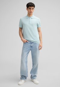 Jasnoniebieska bawełniana koszulka polo z krótkim zapięciem, w połączeniu z jasnymi dżinsami i białymi trampkami. Swobodny krój, gładka tekstura.