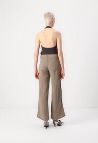 Black sleeveless top with halter neck, paired with light brown wide-leg trousers. Smooth texture with a subtle crinkle pattern. Silver heels.
