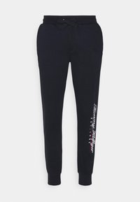 Tmavě modré tepláky vyrobené z bavlněné směsi, s páskem na stažení v pase, zúženými nohavicemi a potiskem "Tommy Hilfiger EST. 1985" na boku.