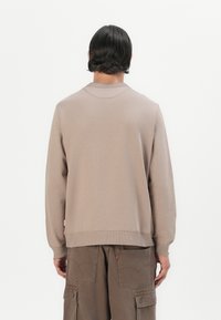 Beige genser med rund hals, ribbede mansjetter og nederkant. Laget av bomull, enkel design. Båret med brune cargo-bukser.