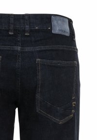 Pantalones vaqueros oscuros con una cintura alta, costuras visibles, dos bolsillos traseros y una etiqueta de cuero en la parte posterior con una marca en relieve.