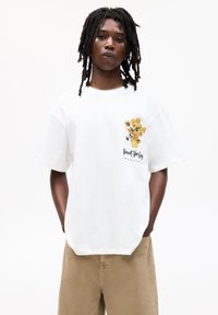Weißes Baumwoll-T-Shirt mit einem bunten Blumentopf-Graphic auf der linken Brust und lockeren kurzen Ärmeln. Lässiges Design mit einer glatten Textur.