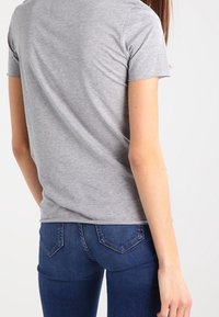 Grå bomullströja med kort ärm, rund halsringning, slät textur. Bärs tillsammans med mörkblå tajta jeans med design på bakfickan.