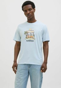 Lichtblauw katoenen t-shirt met korte mouwen, met een grafisch ontwerp aan de voorkant van een strandbar met palmbomen en de tekst "Jack & Jones" onderaan.