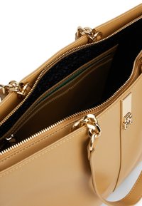 Sac à main en cuir beige avec accessoires dorés, compartiments à double fermeture éclair, doublure noire texturée et une bandoulière réglable.
