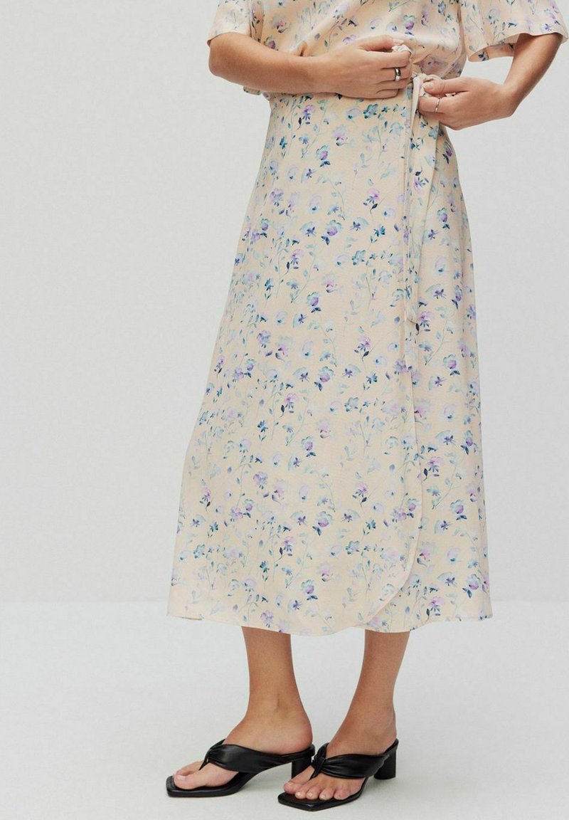 Blommig wrapkjol i ljus persikofärgad tyg med blå och lila blommönster, med en knytning i midjan och en flödande nederkant.