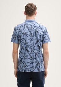 Polo à manches courtes de couleur bleu clair avec un motif de feuilles noires, col et finitions contrastantes le long des manches et de l'ourlet.