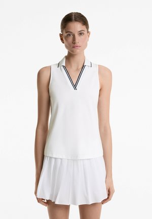 White sleeveless polo top with a V-neck, featuring navy striped accents on the collar. Smooth fabric with a relaxed fit.