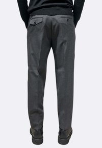 Pantaloni grigi su misura con taglio dritto, piega singola e due tasche posteriori. Indossati con scarpe nere, design minimalista.