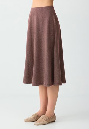 Jupe trapèze longueur genou en tissu marron texturé portée avec des mocassins en daim beige sur un mannequin devant un fond uni.