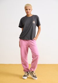 Grey cotton t-shirt with short sleeves and a graphic design on the front, paired with pink fleece pants featuring pockets and elastic cuffs.