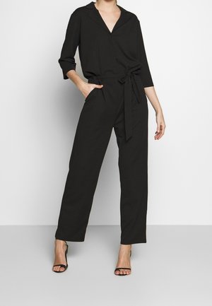 Czarny kombinezon z wyciętym kołnierzem, długimi rękawami, wiązanym w pasie oraz bocznymi kieszeniami. Gładki materiał o prostym kroju nogawki i luźnym fasonie.