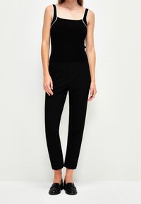 Svart linne med vit kant, parat med svarta skräddarsydda byxor. Outfiten har en figursydd design och slät textur. Svarta loafers fulländar looken.