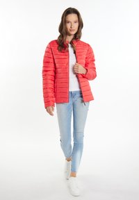 Rød pufferjakke med et cropped design, der har vandrette quiltede sektioner og en ståkrave, parret med lyseblå skinny jeans.