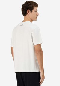 T-shirt bianco in cotone con maniche corte, taglio dritto e un piccolo logo nero sulla parte posteriore del colletto. Tessuto liscio e design casual.