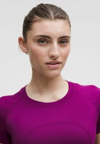 Kohandatud lühikeste varrukatega särk elava lilla värviga, millel on tekstuuriga kangas ja ümmargune kaelus. Näha on lihtsad metallkõrvarõngad ja õrn kaelakee.