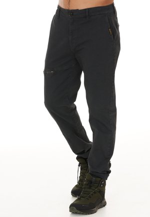 Pantalons cargo noirs avec une fermeture à bouton et des poches latérales zippées. Coupe fuselée, fabriqués à partir d'un matériau durable, associés à des bottes de randonnée sombres.