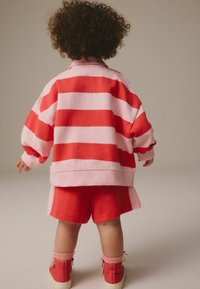 Sweatshirt oversize rayé rouge et rose avec un short rouge assorti, accompagné de baskets montantes rouges et de chaussettes roses à la cheville.
