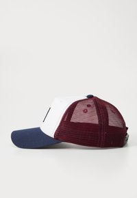Casquette de baseball avec un devant blanc, une visière bleu marine et un dos en maille bordeaux. Présente un design de couleur unie et des trous de ventilation. Aucune logo visible.