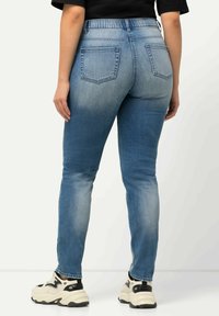 Pantalones vaqueros ajustados de color azul con una textura desvaída, bolsillos traseros y una cintura alta, combinados con zapatillas gruesas en blanco y negro.
