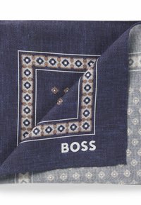 Dark blue scarf with geometric patterns and a white border. Features logo "BOSS" in white. Smooth texture, folded corner reveals layered design.