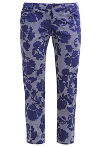 Blå mönstrade byxor med en blommönstring och en strukturerad yta, som kontrasterar med en ljusare, rutmönstrad bakgrund.