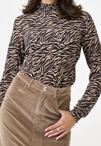 Långärmad topp i beige med svarta zebramönster, med en volangkrage. Matchad med en strukturerad, ljusbrun corduroyklänning.