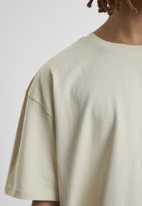 Beige, rövid ujjú póló, puha pamutból készült, laza szabású, klasszikus kerek nyakkivágással és diszkrét textúrával.