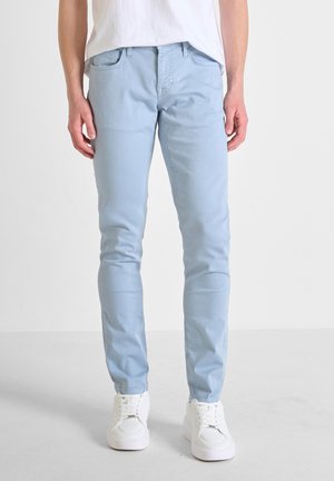 Light blue slim-fit jeans made of denim, featuring five pockets, belt loops, and a smooth texture, paired with white sneakers.