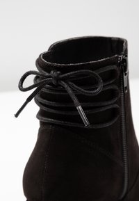 Stivale alla caviglia in suede nero con zip laterale e lacci decorativi annodati a fiocco sul colletto posteriore.