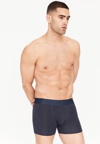 Marinefarbene Boxer-Shorts aus dehnbarem Material, mit einem glatten Bund und geprägtem Logo. Das Design hat eine enganliegende Form und minimalen Nähten.