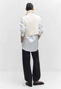 Witte geribbelde cropped trui over een lichtblauw shirt met lange mouwen, gecombineerd met zwarte wijde broekspijpen en zwarte platte schoenen.