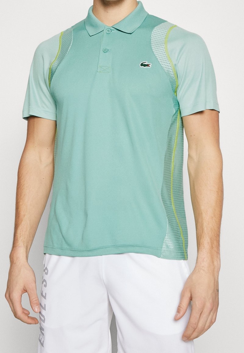 Polo en vert d'eau clair en tissu respirant. Doté de manches courtes, d'un col et d'accents en mesh avec des détails en vert citron. Logo Lacoste présent.