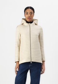 Beige hoodie met een gewatteerd ontwerp, voorzien van verticale strepen, een ritssluiting aan de voorkant en een slanke pasvorm, gecombineerd met denim jeans.