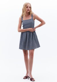 Sininen ja valkoinen ruudullinen mekko, jossa on neliönmuotoinen pääntie, leveät olkaimet ja liehuva hame. Sileä kangas, jossa on kevyt pinta, polvipituisena.