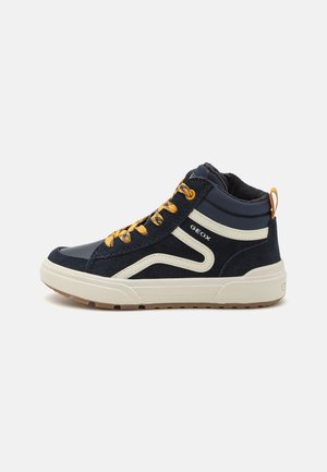 Sneaker alte con esterno in suede blu navy, dettagli color crema e lacci gialli. Presentano una suola in gomma testurizzata e una linguetta sul retro.