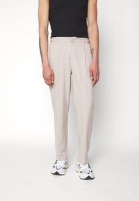 Beiga skräddarsydda byxor med en slät textur, sidofickor och rak skärning, kombinerat med vita och svarta sneakers och en åtsittande svart linne.