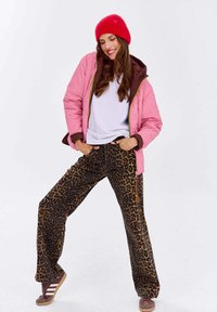 Różowa i brązowa kurtka z wypełnieniem, biała koszula i spodnie w leopardzi wzór o luźnym kroju. Czerwony beanie i brązowe buty dopełniają strój.