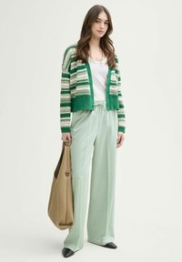 Cárdigan de punto con rayas en verde y crema, top blanco, pantalones anchos en menta clara y una bolsa de mano beige contra un fondo neutro.