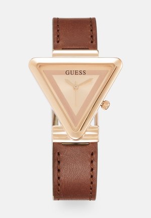 Montre-bracelet Guess triangulaire en ton or avec cadran beige, trois aiguilles dorées et bracelet en cuir marron avec coutures visibles.