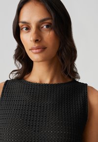 Abito nero lavorato a maglia con scollatura rotonda, texture a rete aperta e senza maniche. Il tessuto presenta un motivo strutturato con spaziatura uniforme.