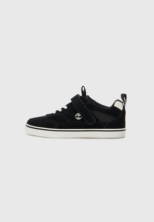 Baskets en daim noir avec une semelle en caoutchouc blanche, bande velcro et accents en lacet ; présente un logo sur le côté et un renfort de talon en contraste.
