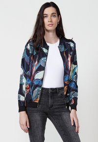 Giacca bomber con motivo floreale su sfondo nero, realizzata in tessuto liscia, con colletto e polsini a coste, chiusura con zip e tasche laterali.